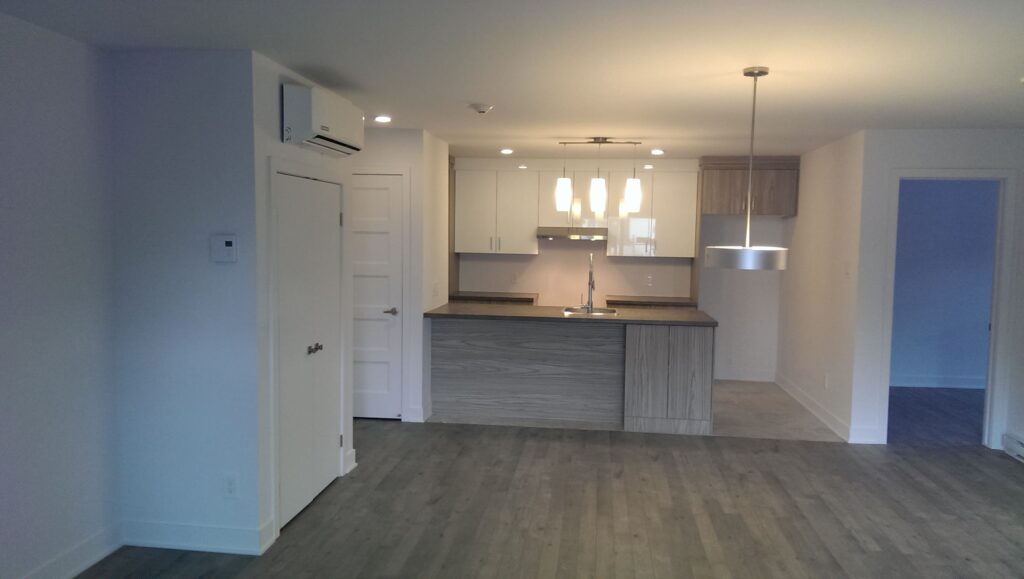 Intérieur d’un appartement contemporain avec cuisine ouverte, îlot central en finition bois et éclairage suspendu.