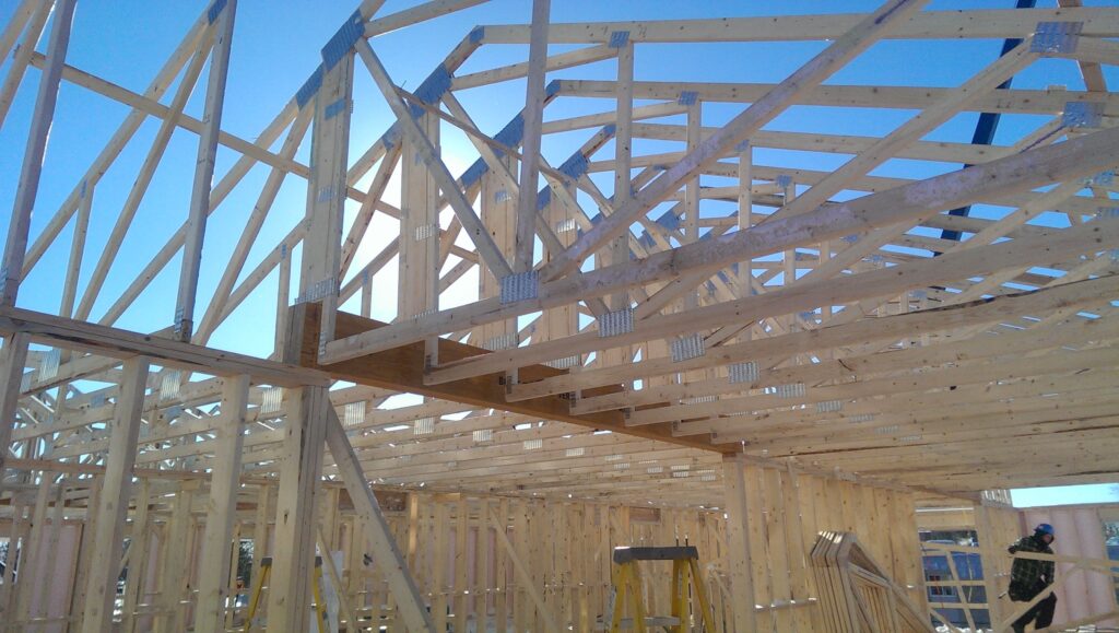 Structure de toit en bois avec fermes assemblées et connecteurs métalliques sous un ciel bleu, en pleine construction.