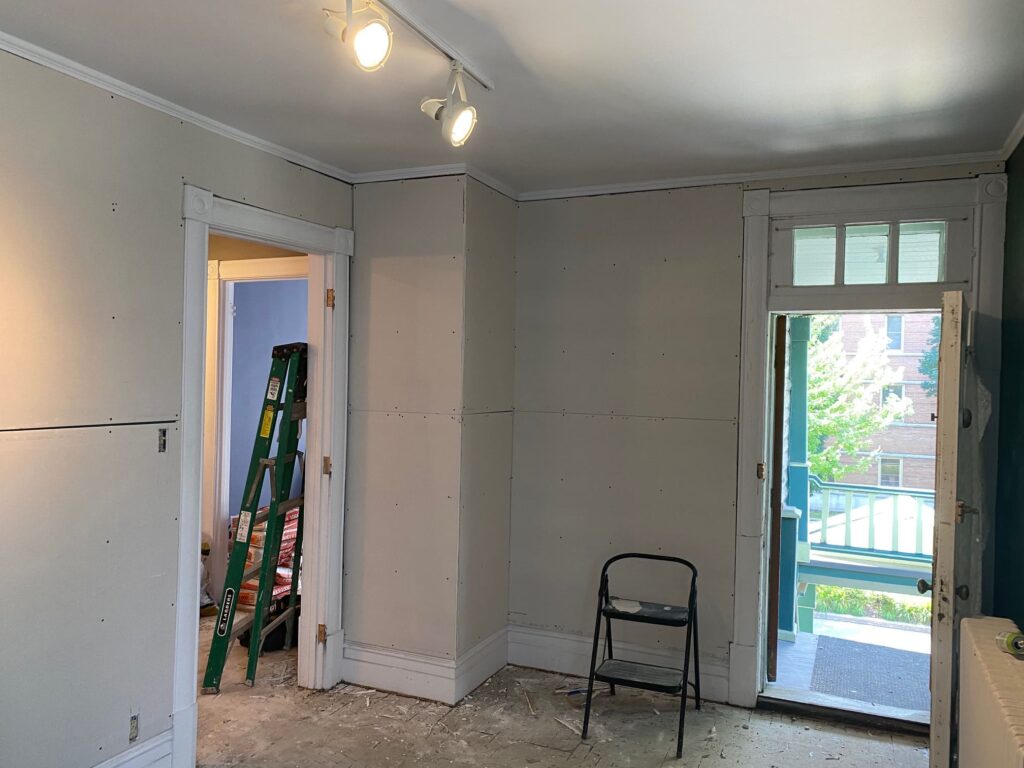 Chambre en rénovation avec des murs en gypse récemment posés, une porte ouverte menant à un balcon, et des outils de travail.